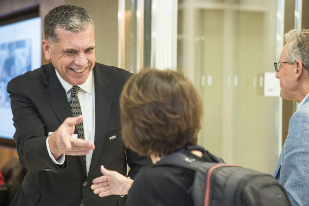 DRA Board member Barry Taylor smiling and reaching out to shake hands with another guest while another guest walks behind them.