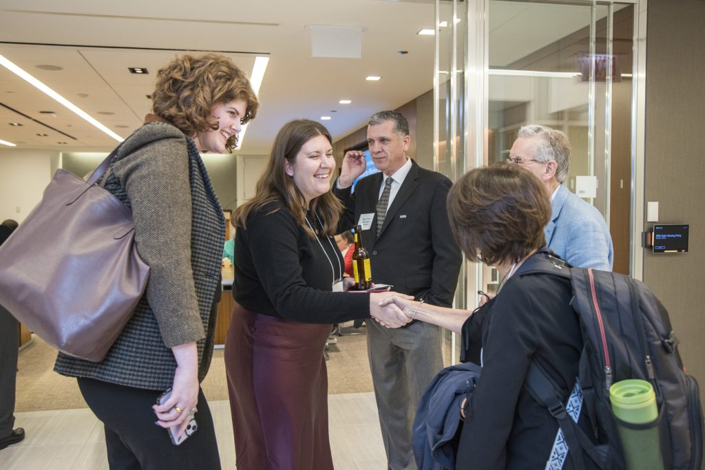 DRA's Emily Roznowski smiling and shaking hands with a guest while two other guests and DRA Board member Barry Taylor watch.