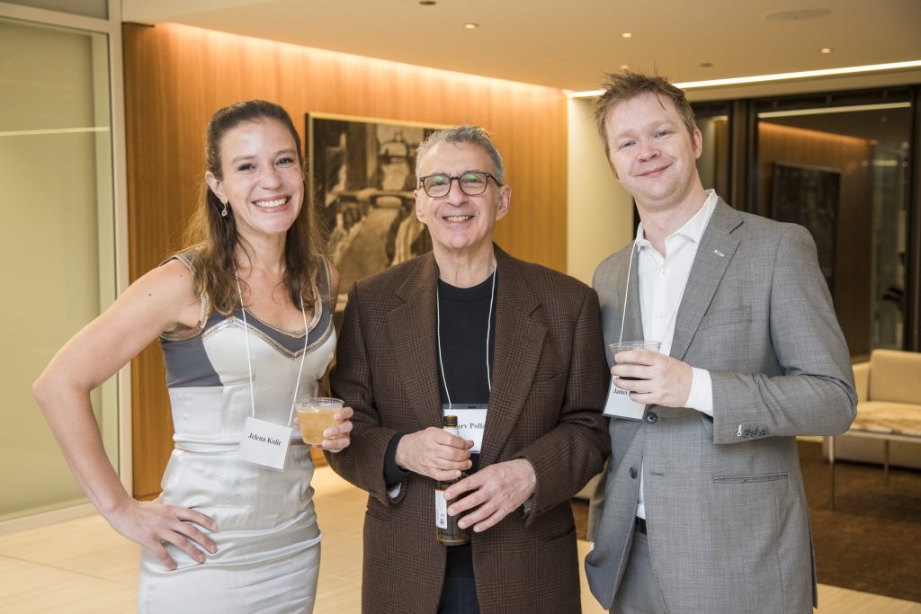 Three guests posing and smiling. A picture of a bridge over a river is hanging on the wall behind them.