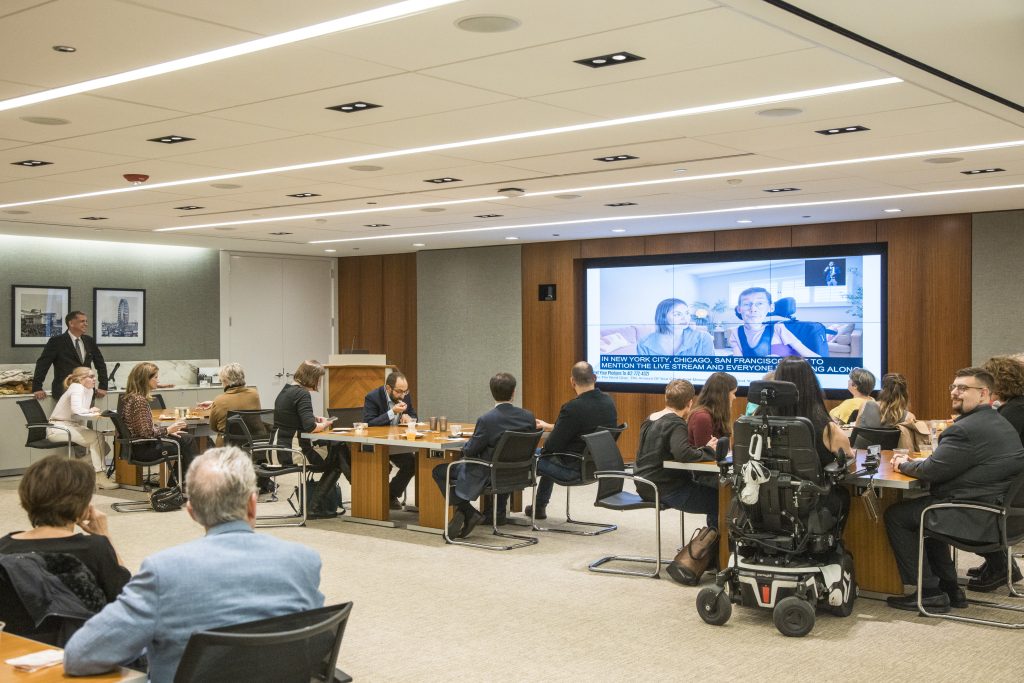Many guests seated at tables watching the on-screen program that is currently displaying DRA board member Shane Burcaw and his wife Hannah Burcaw.