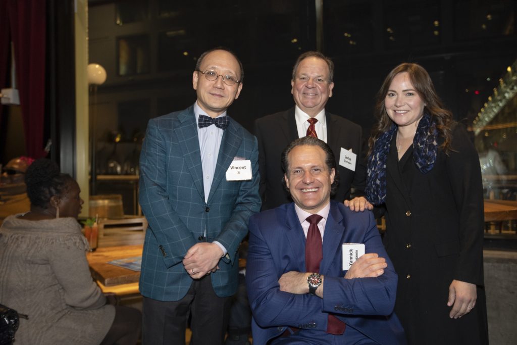 Honoree Yannick Benjamin posing and smiling with three guests. Yannick is using a wheelchair and the other three guests are standing behind him. Another guest can be seen sitting at a table behind them.