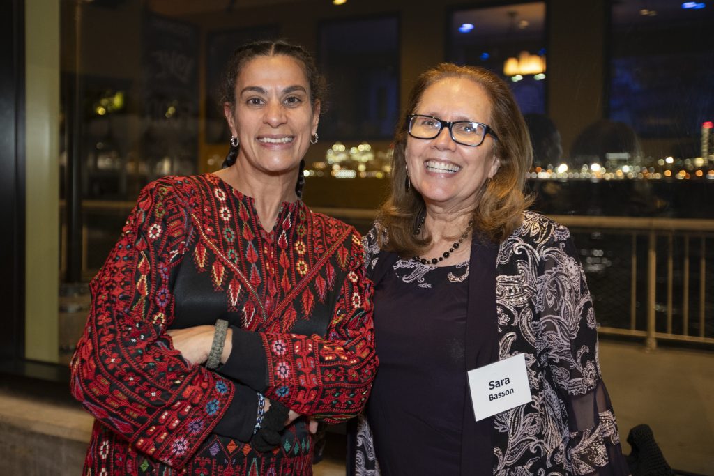 Two guests posing and smiling. City lights can be seen through the window behind them.