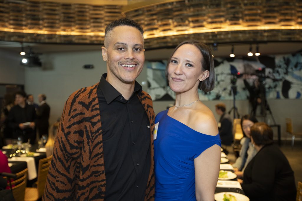 DRA Board member James Ian posing with a guest, both smiling. Other guests are talking in the background.