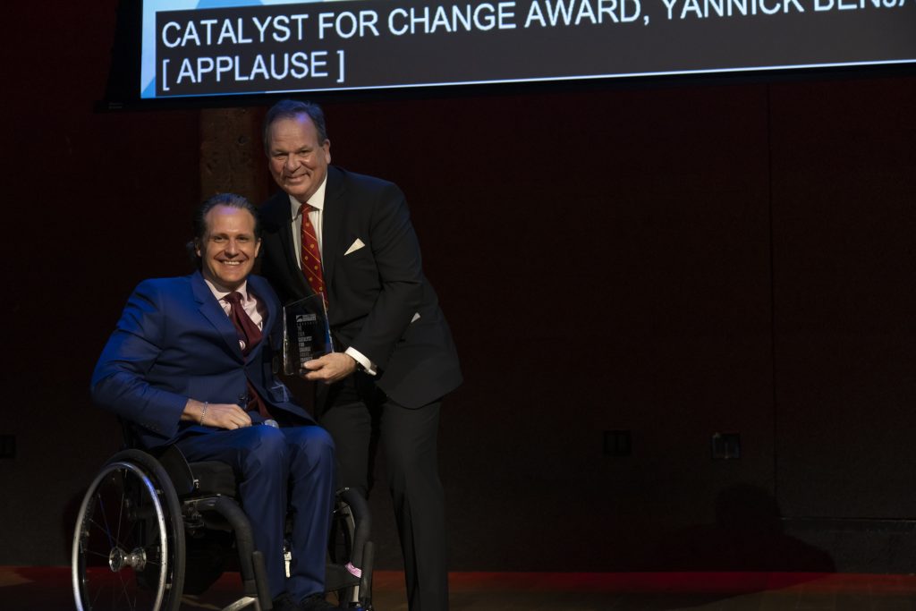 Special guest John Dorman presenting an award on stage to honoree Yannick Benjamin, who is using his wheelchair.