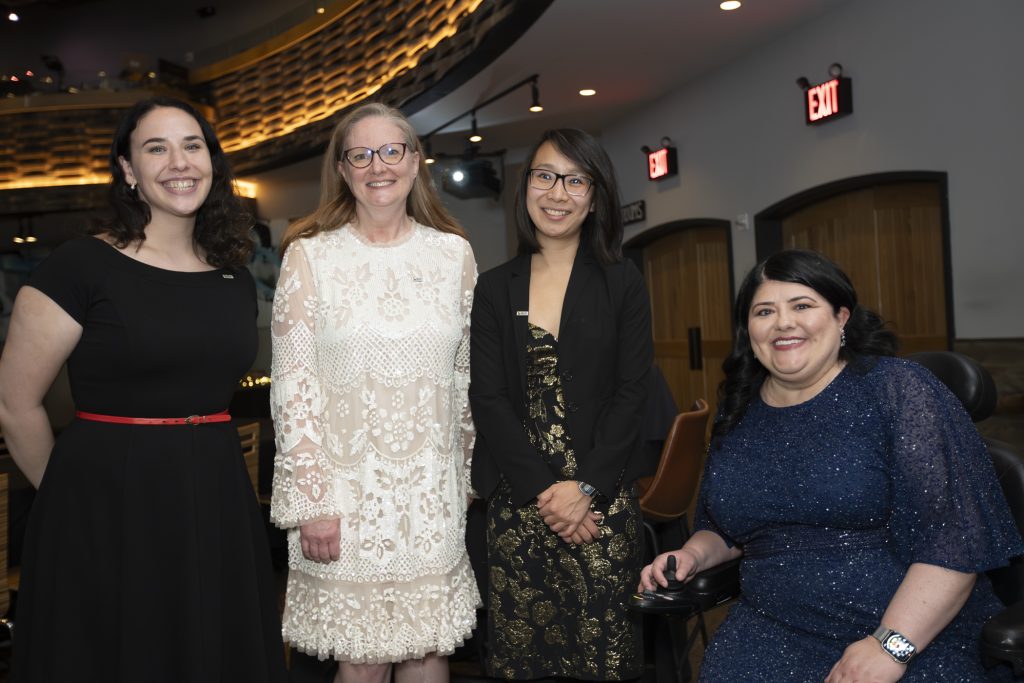 DRA's Eliana Fisher, Aileen Parker, Elizabeth Gyori, and Rebecca Williford posing and smiling. Rebecca is using a wheelchair.
