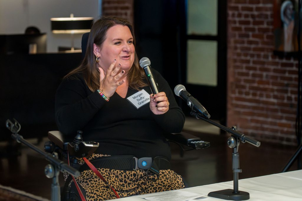 DRA Board member Morgan Duffy-Granville speaking into the microphone she is holding while gesturing with her hand.