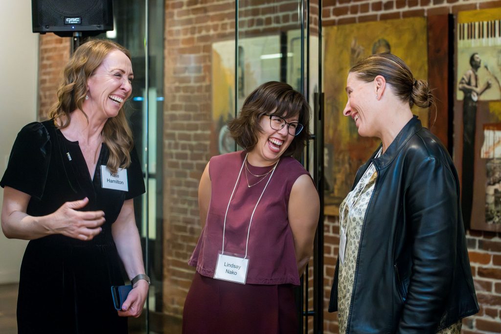 DRA's Kate Hamilton and DRA Advisory Board member Anya Emerson laughing with a guest in front of a brick wall.