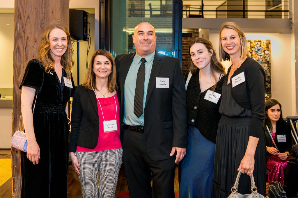 DRA's Kate Hamilton posing with four guests, all smiling. Another guest is seated behind them.