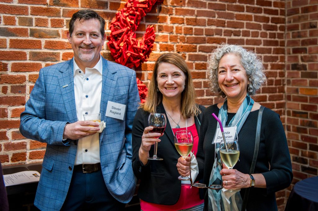 DRA Board member Steven Ragland and DRA Advisory Board member Linda Dardarian pose with a guest, all smiling, in front of a brick wall.