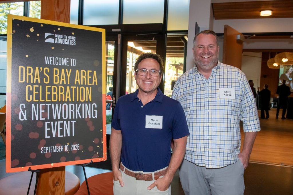 Two event guests smiling next to a sign reading "Welcome to DRA's Bay Area Celebration & Networking Event"
